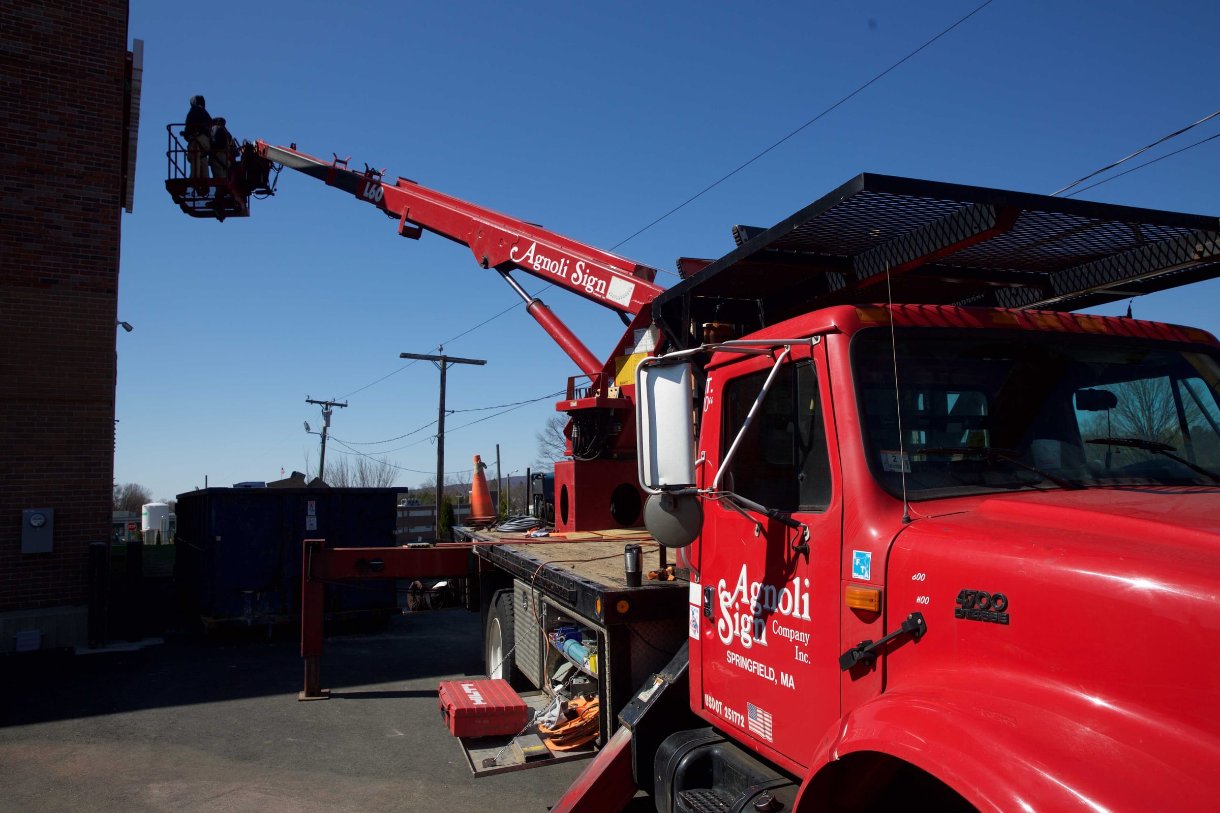 The red Agnoli Sign boom truck at a job, a two-man crew in the bucket at the top of a brick building