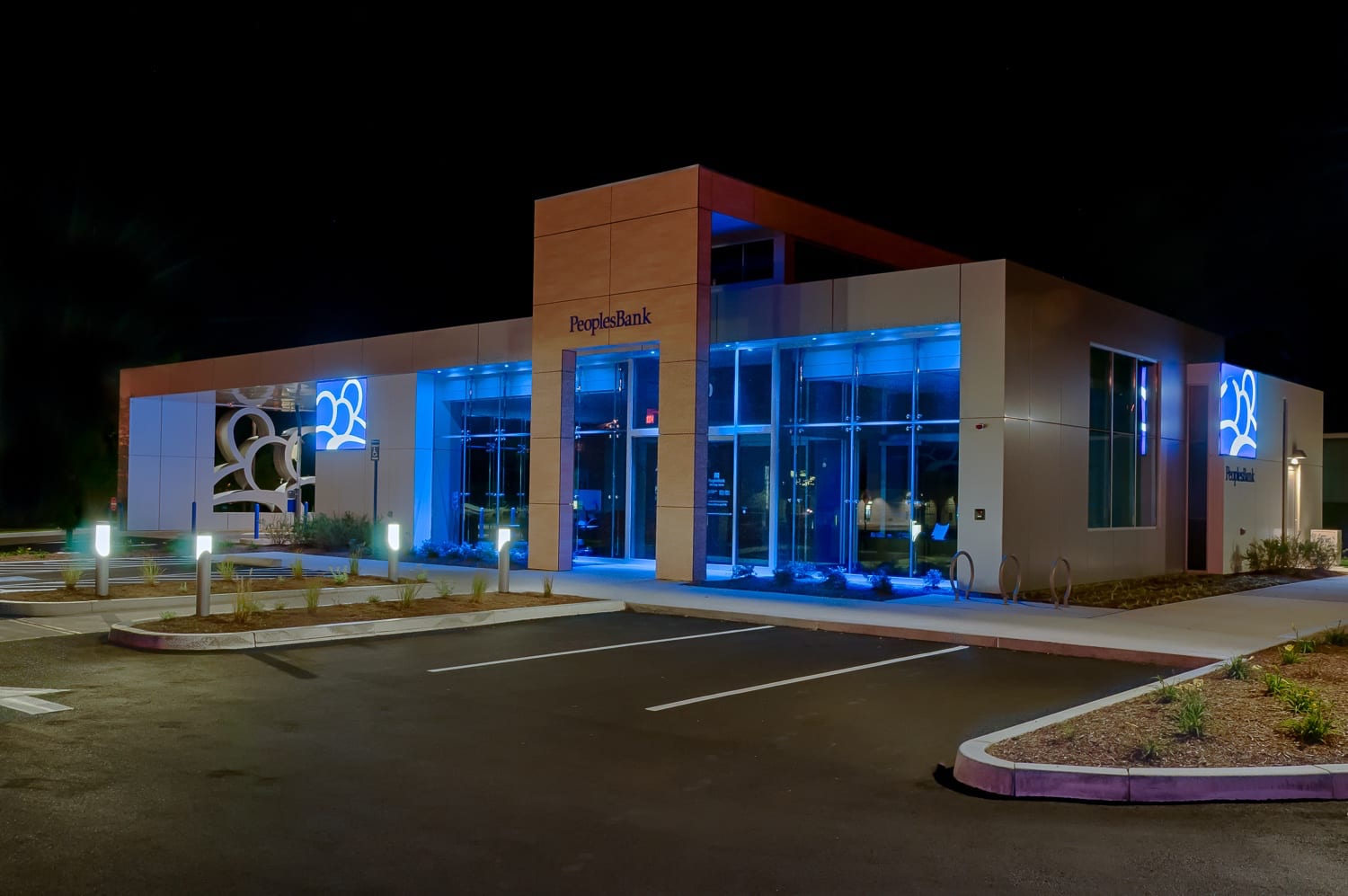 Modern bank building at night with blue lighting and an illuminated sign