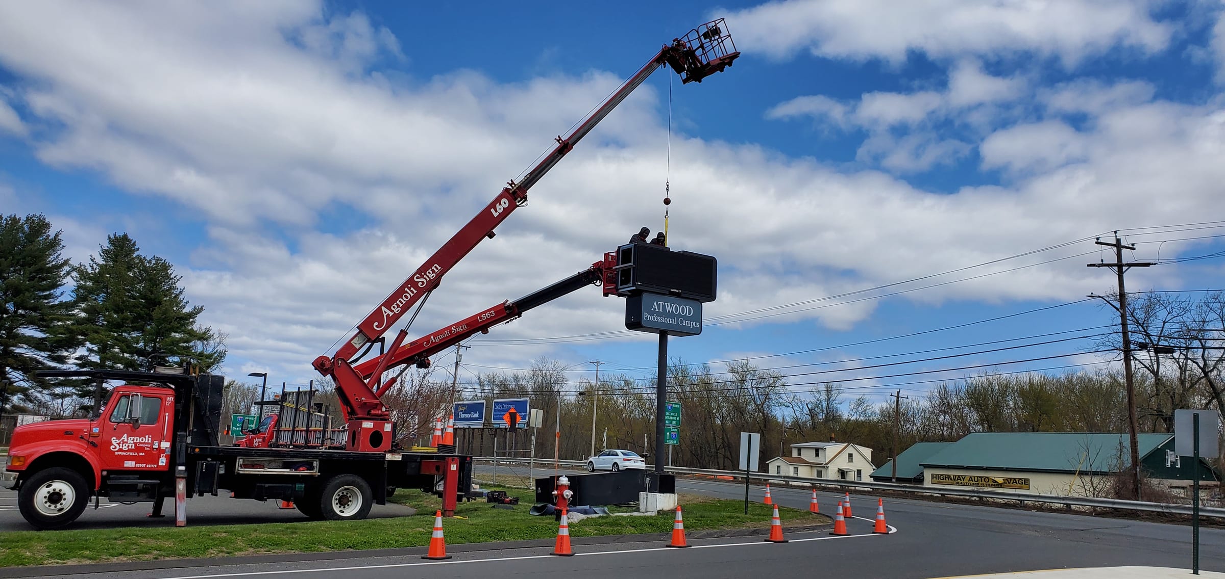 Agnoli boom truck lifting a pylon sign with an electronic message center into place, cones out on the roadside