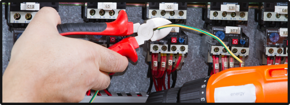 Close-up of a hand cutting a wire with red-handled linesman&rsquo;s pliers across a row of DIN-rail contactors