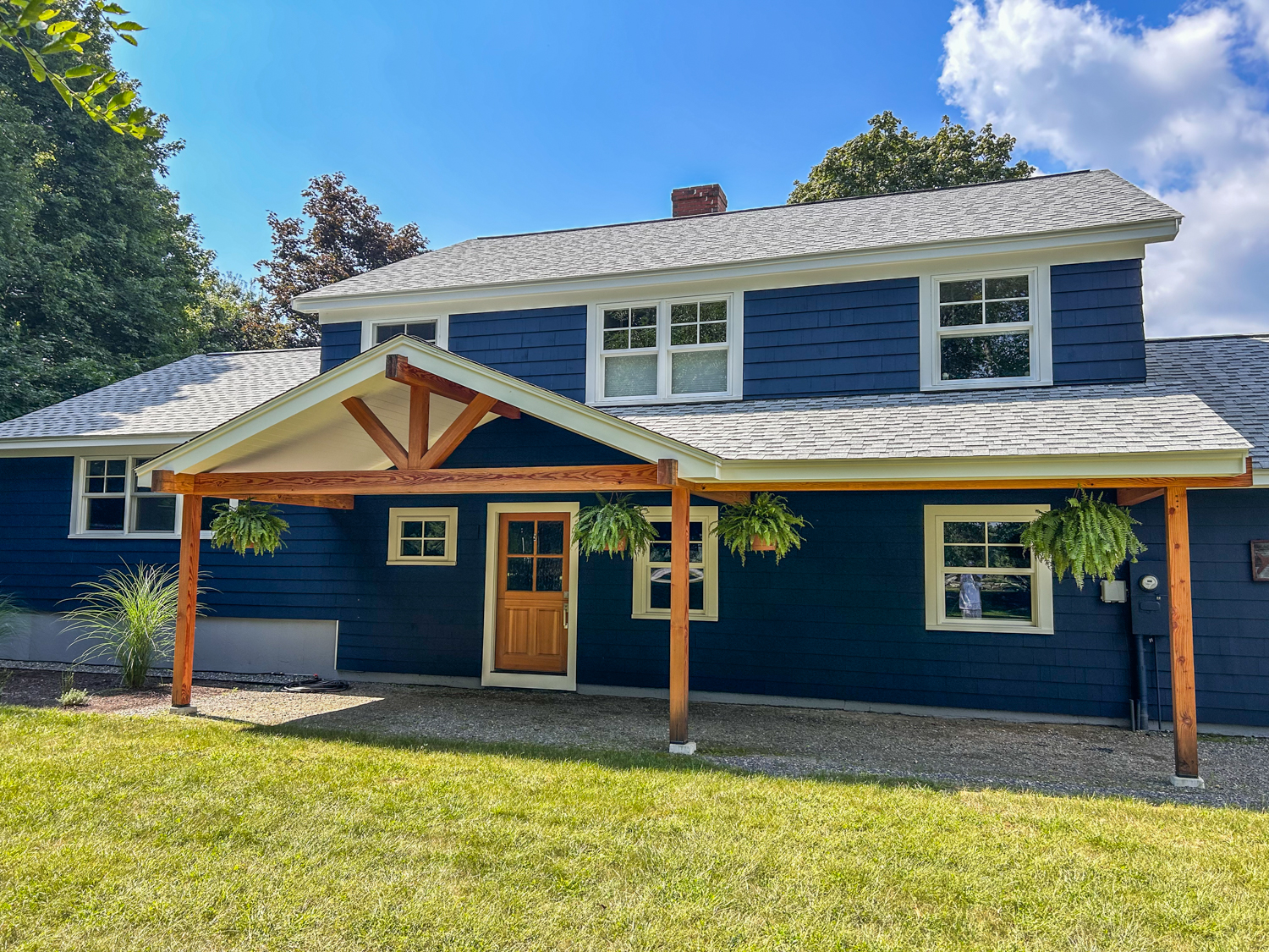 A navy clapboard house with cream trim and a new heavy timber post and beam covered entry porch