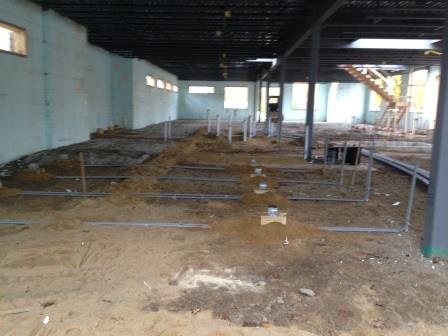 Conduit sweeps running across the dirt floor of a steel frame building before the slab is poured