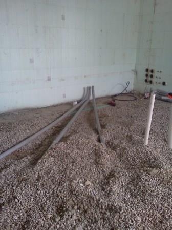 A conduit run crossing a dirt floor toward an interior wall