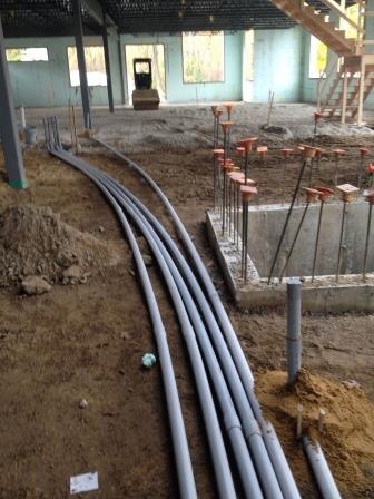 A bundle of conduit sweeps rising out of the dirt floor of a building under construction