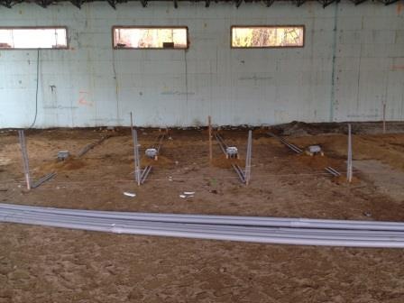 Conduit runs laid across a dirt floor with column stubs already set