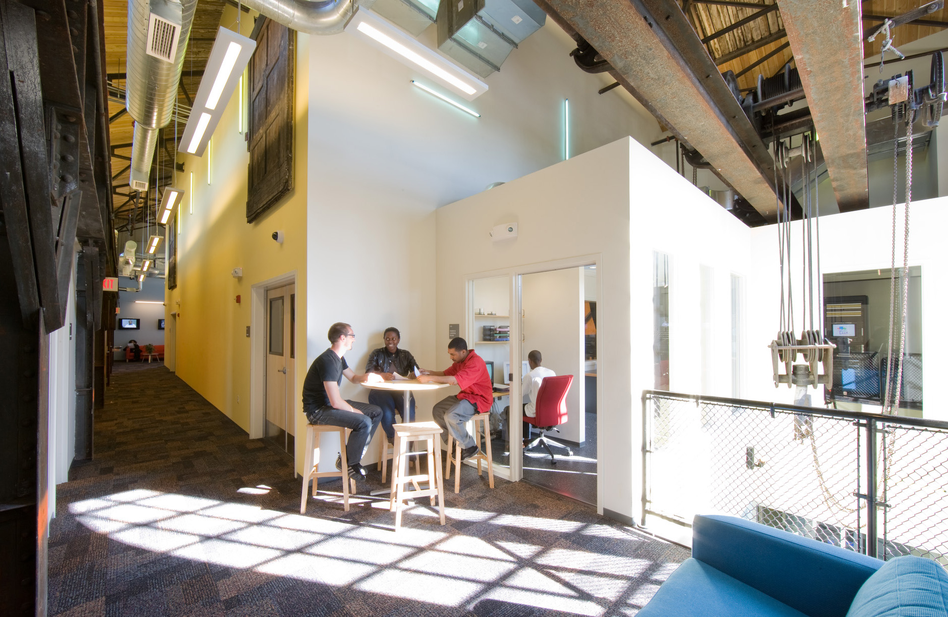 Second-floor lightwell at the BNN TV Studio in Roxbury: exposed riveted steel, historic wood roof deck and daylight falling deep across the floor