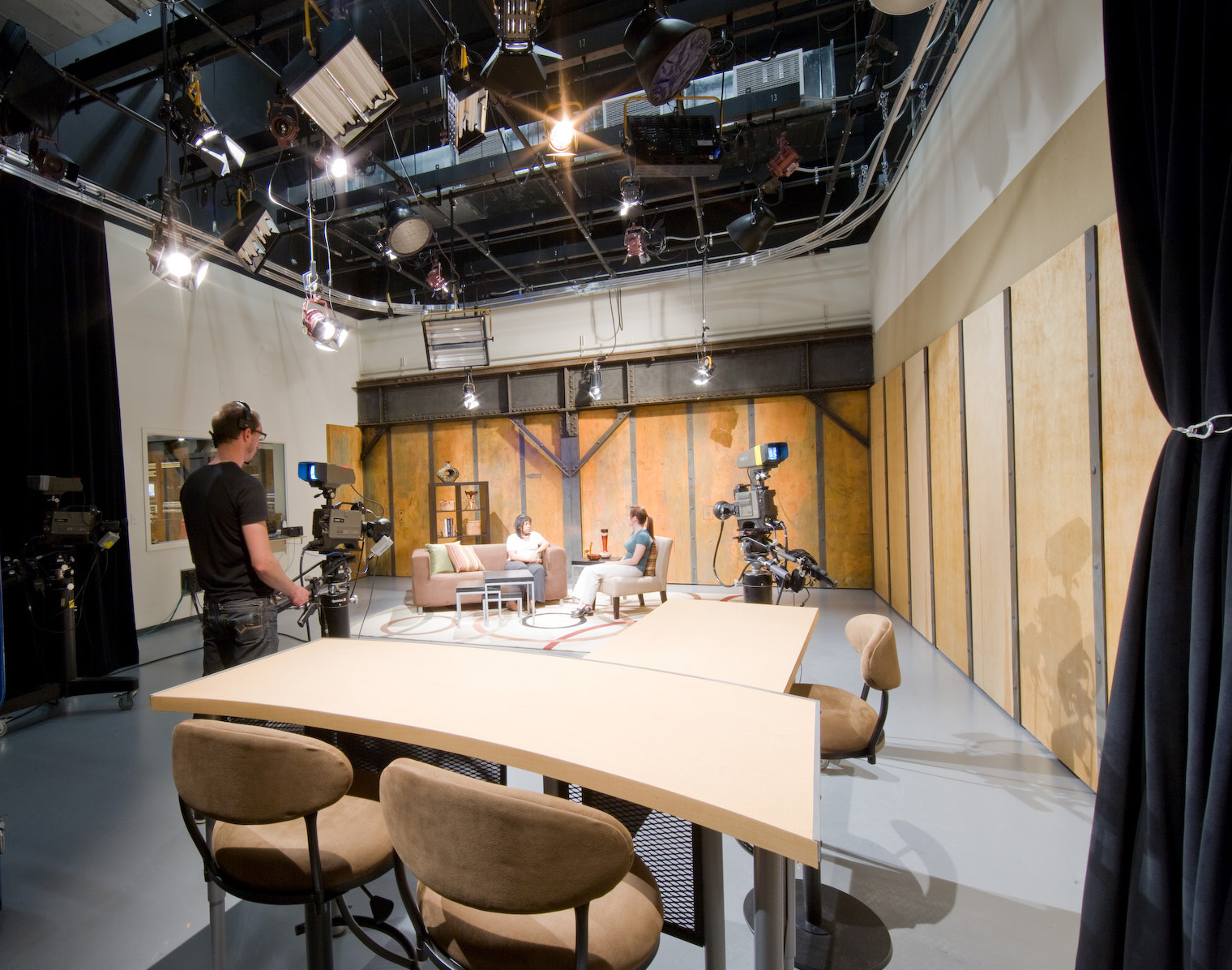 The television studio: overhead lighting grid, cameras and an interview set against exposed riveted steel and plywood