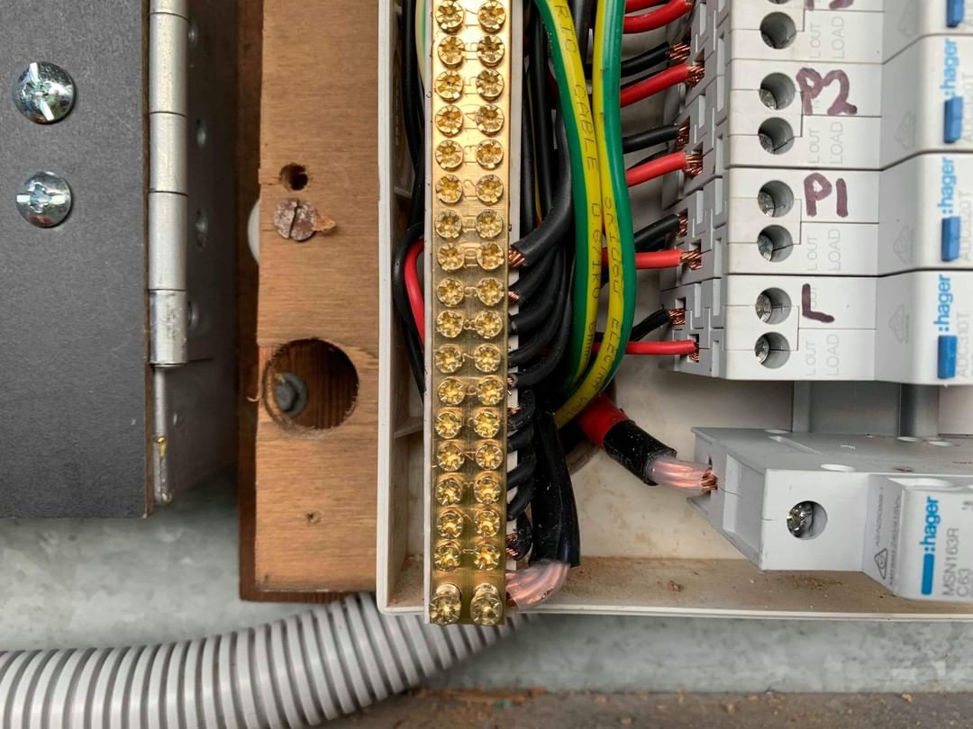 An electrical panel with the door swung open on its hinge, showing a brass neutral bar, color-coded conductors and a row of breakers.