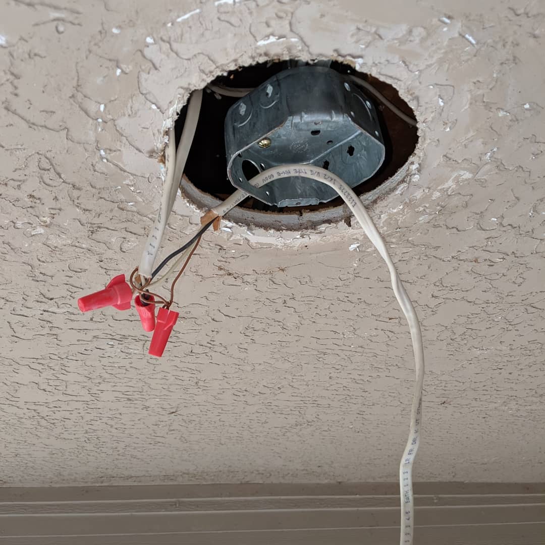 A metal ceiling box hung through an opened hole in a plaster ceiling, with cable and red wire nuts hanging below.