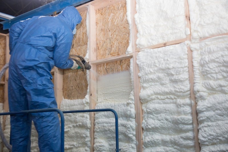 Technician in a protective suit spraying foam insulation into a stud bay