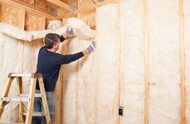 Installer on a step ladder fitting batt insulation between wall studs