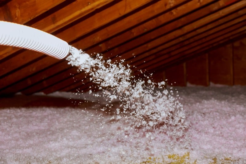 Blown-in cellulose insulation pouring from a hose across an attic floor