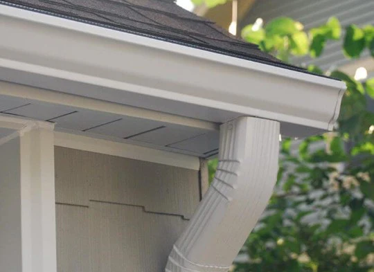 White gutter and downspout fitted along a shingled eave