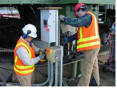 Two electricians in high visibility vests working inside an opened disconnect enclosure on a structure