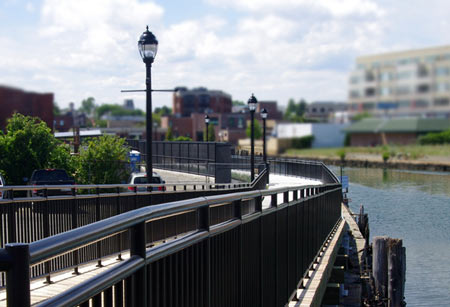 A waterfront walkway with railing and lamp posts running along the harbor