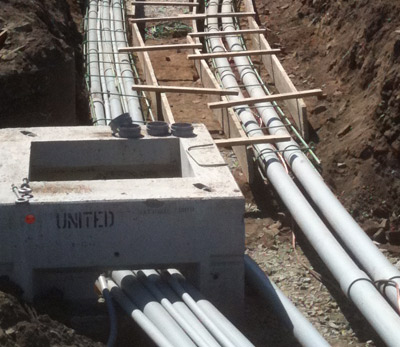Conduits racked on rebar supports running into a precast concrete vault in a trench