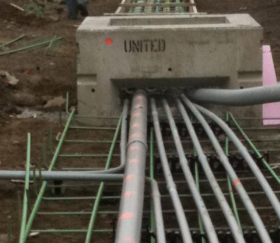 A bank of conduits running into a precast concrete vault in an open trench