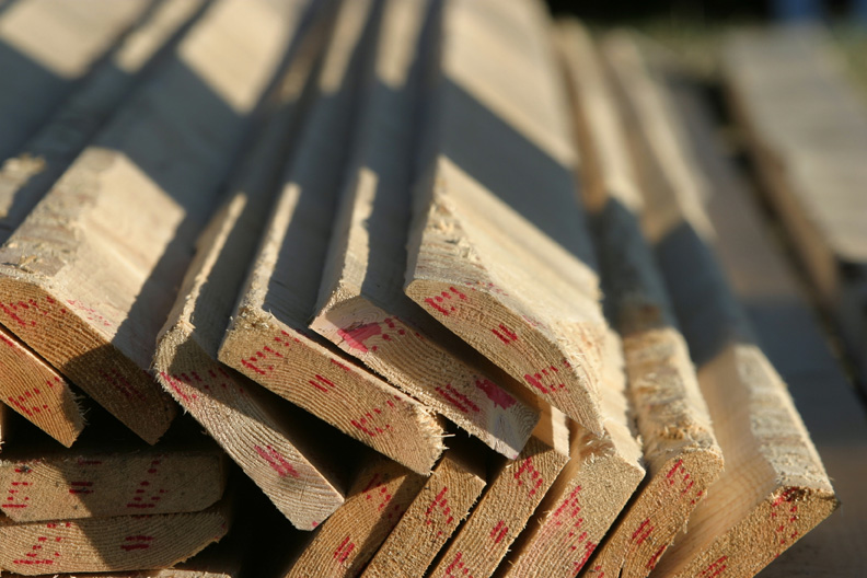 Stacked dimensional lumber marked in red crayon, lit by low sun