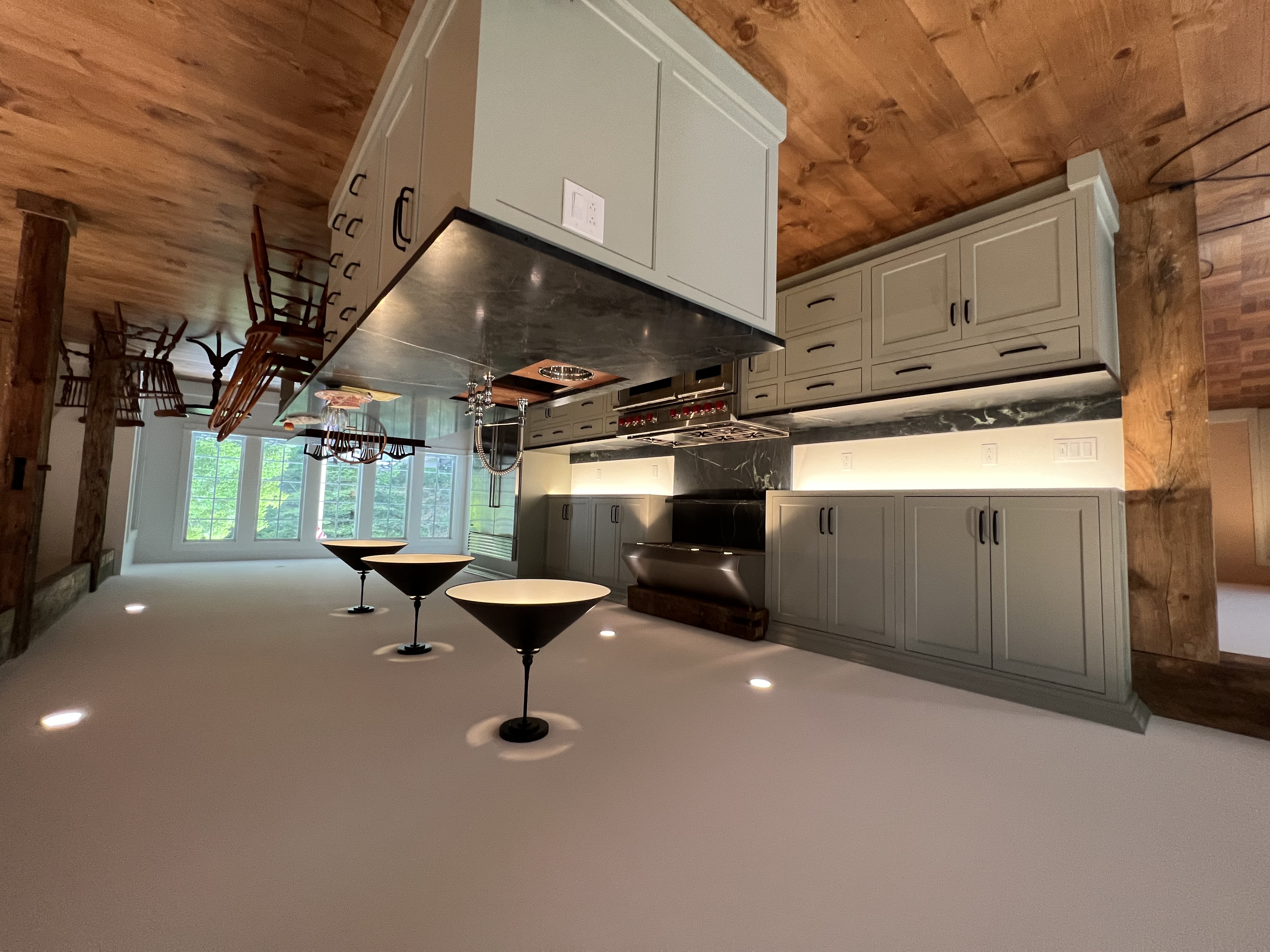 Finished kitchen with pale cabinetry, a long dark stone island, black dome pendants and wide oak floors