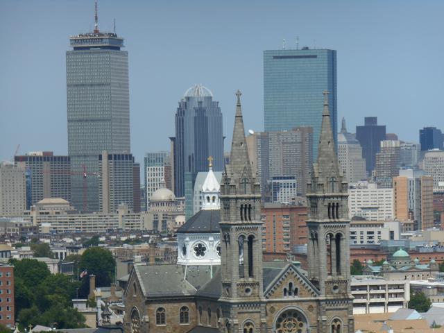 The Boston skyline seen from Greater Boston, with downtown towers behind a stone church