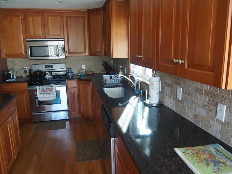 Finished kitchen with cherry cabinets, dark granite counters and a stone tile backsplash