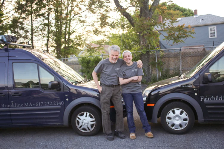 Robert and Julia Fairchild standing arm in arm in front of their two work vans