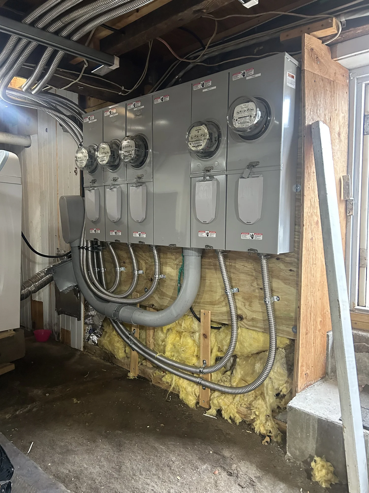 A bank of five electric meters and conduit in an unfinished basement