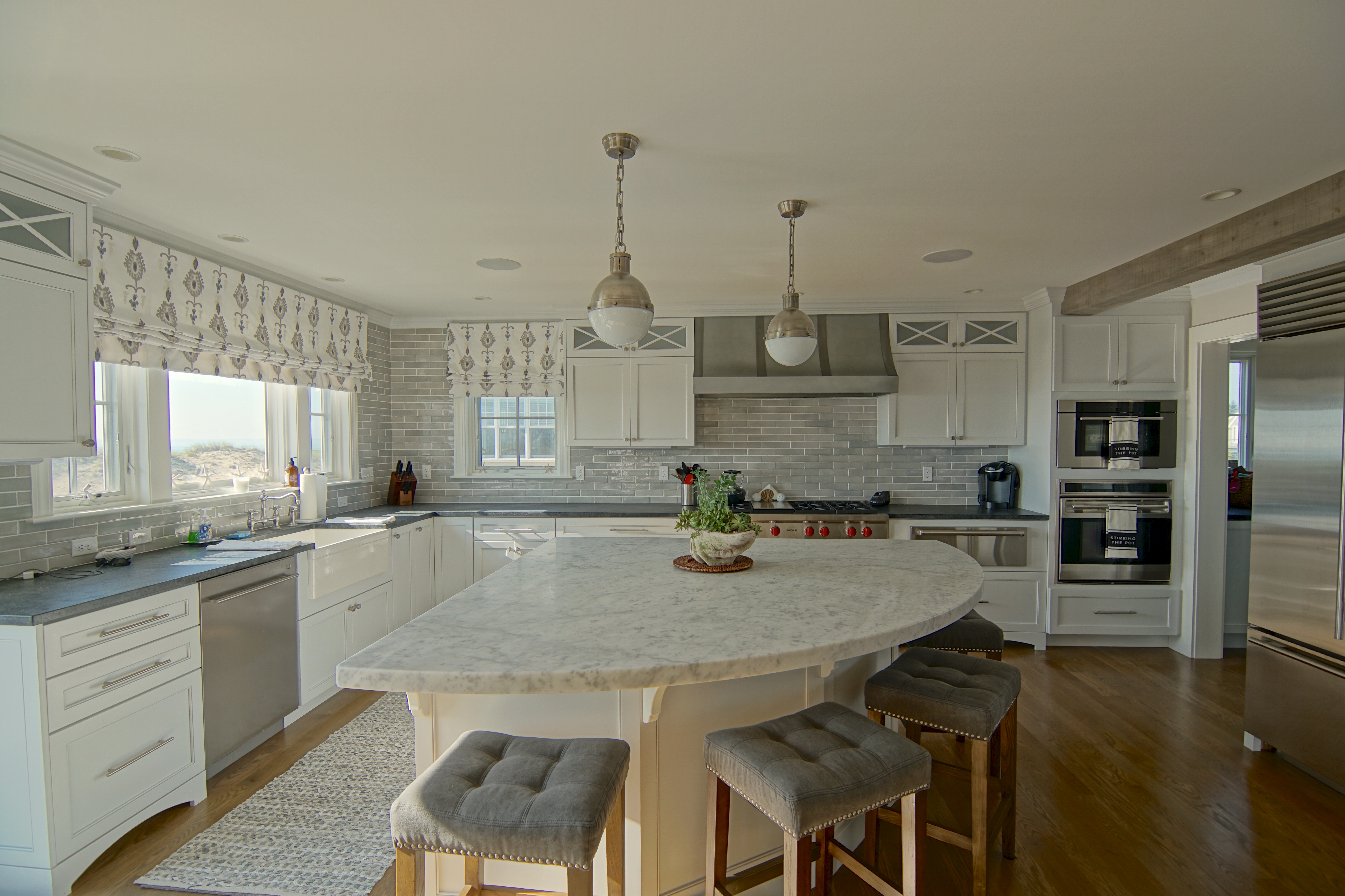 A white custom kitchen with a marble waterfall island, three stools and pendant lights.