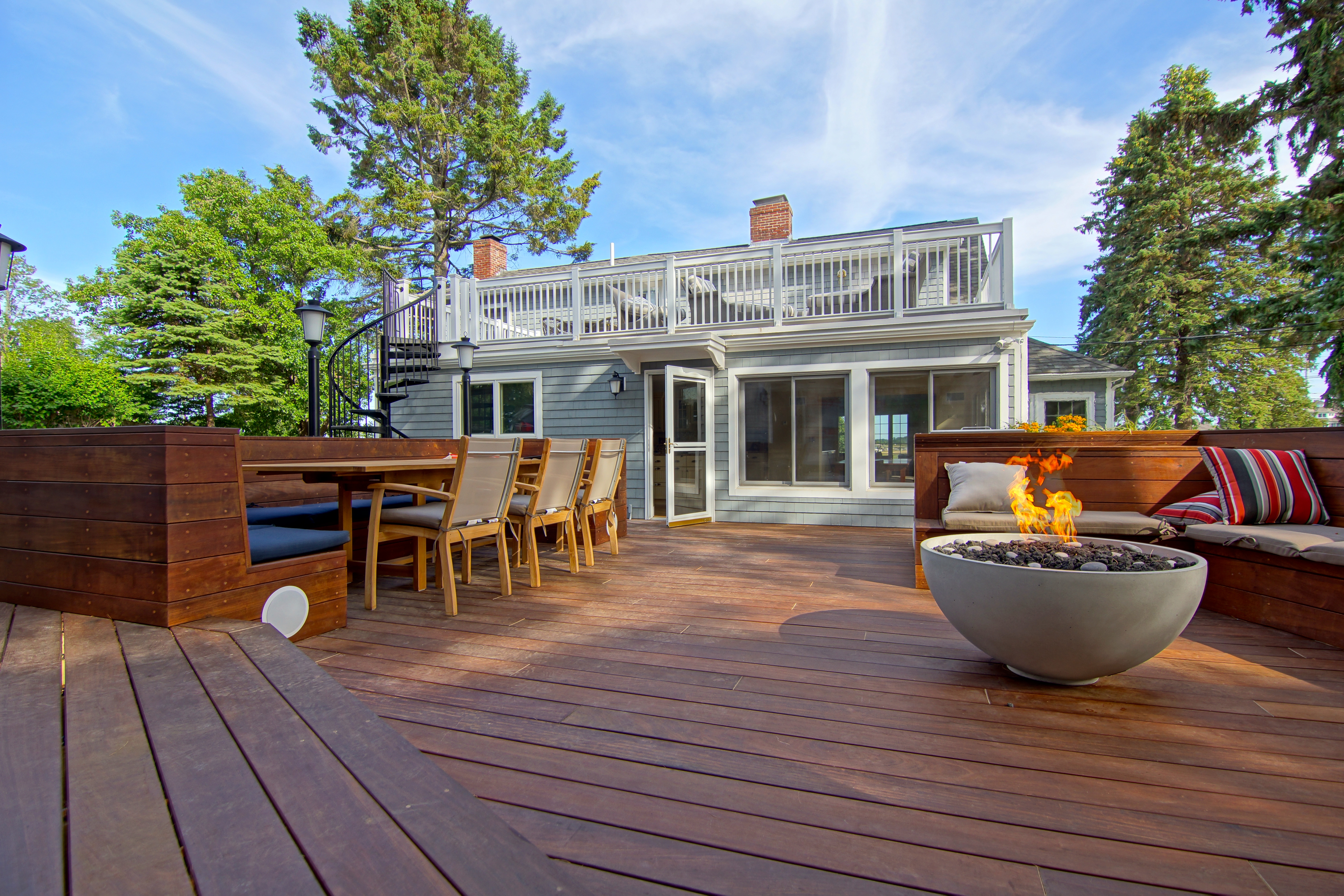 An oceanside hardwood deck built by Gray Construction, with a built-in bench and a lit stone fire bowl.