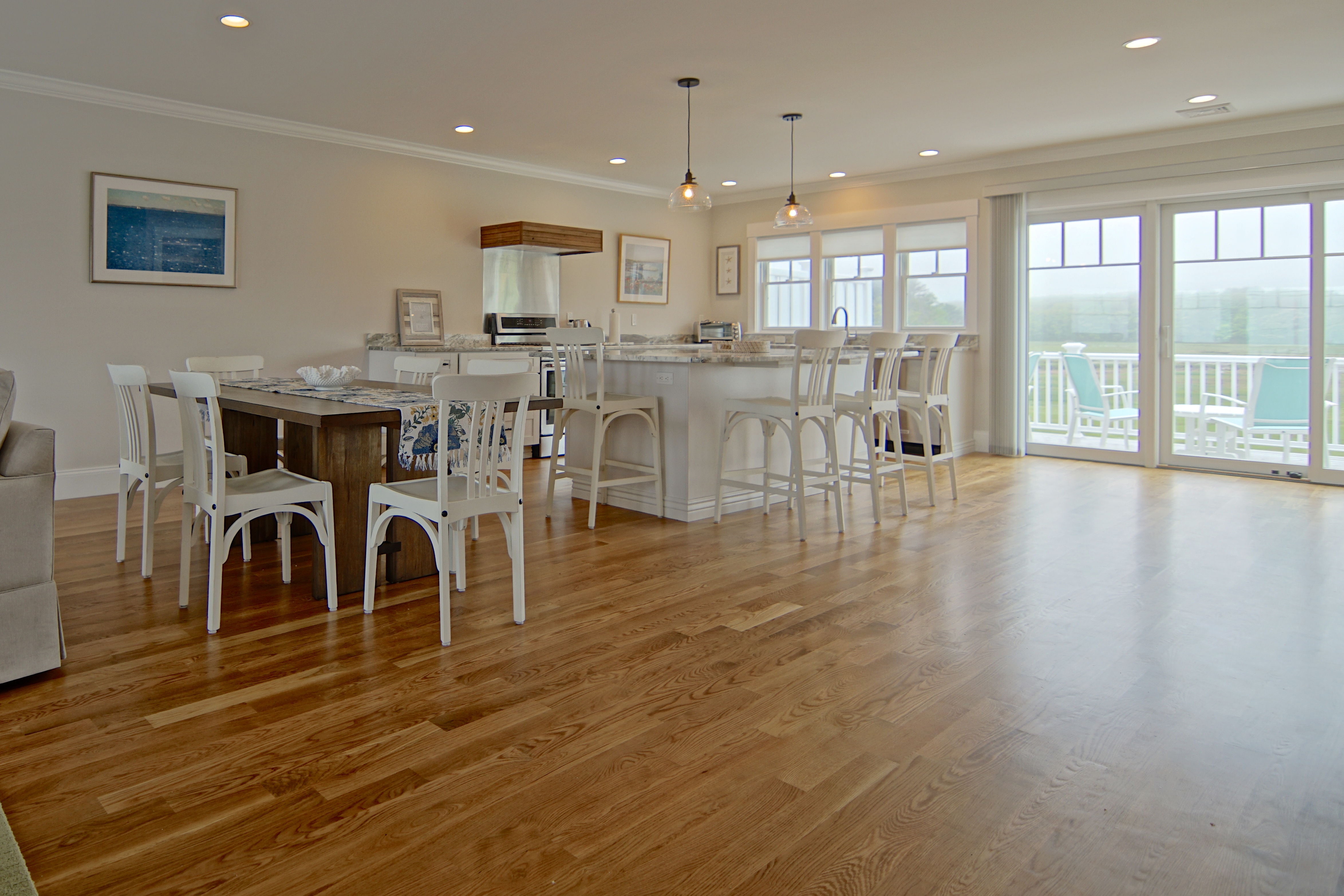 A white kitchen and dining area on wide oak floors, with glass doors opening to the water.