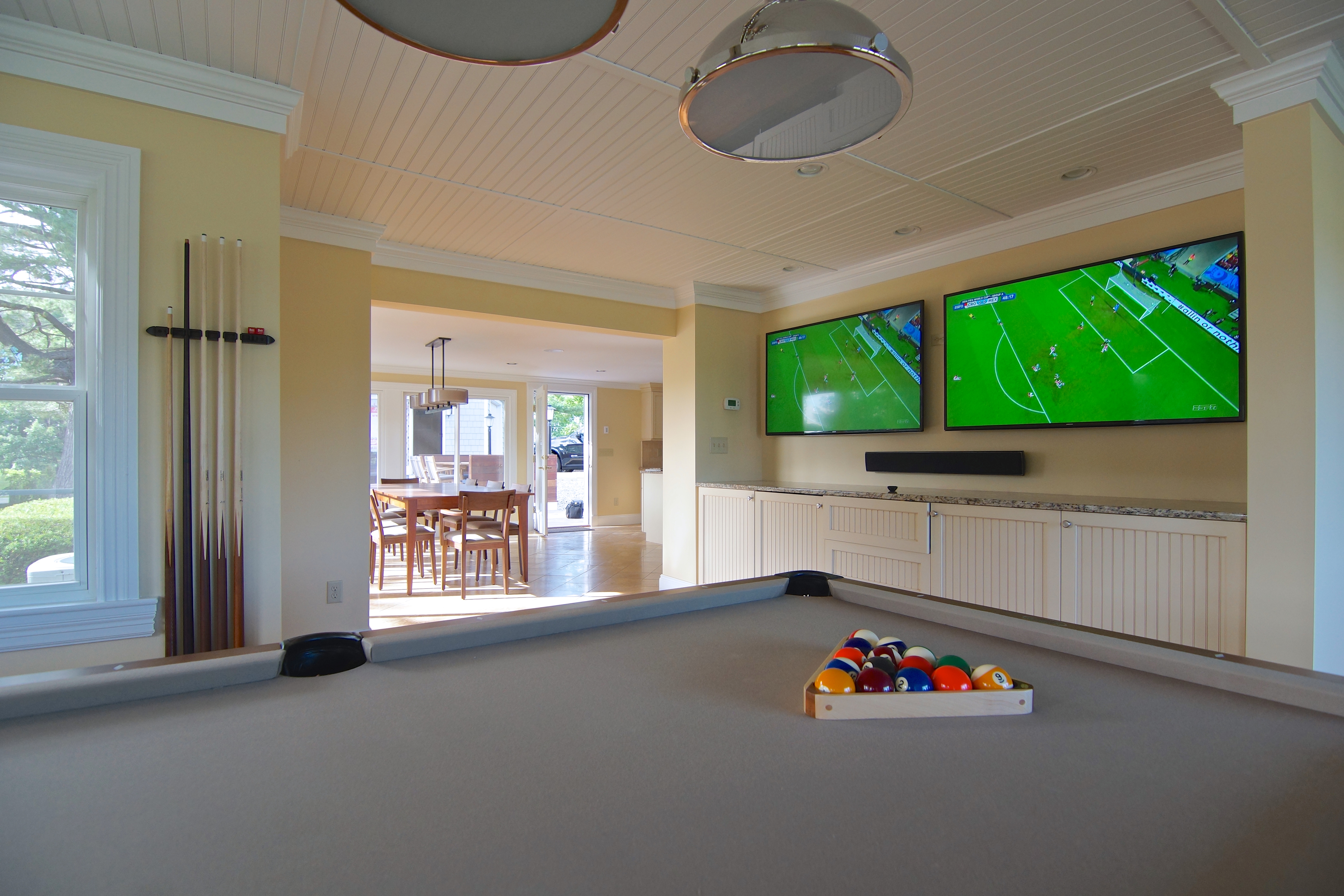 A living room with a pool table and wall-mounted screens, opening through to the dining area.
