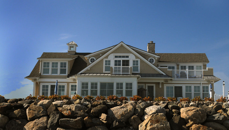 A shingle-style seacoast home built on a granite revetment under a clear sky.