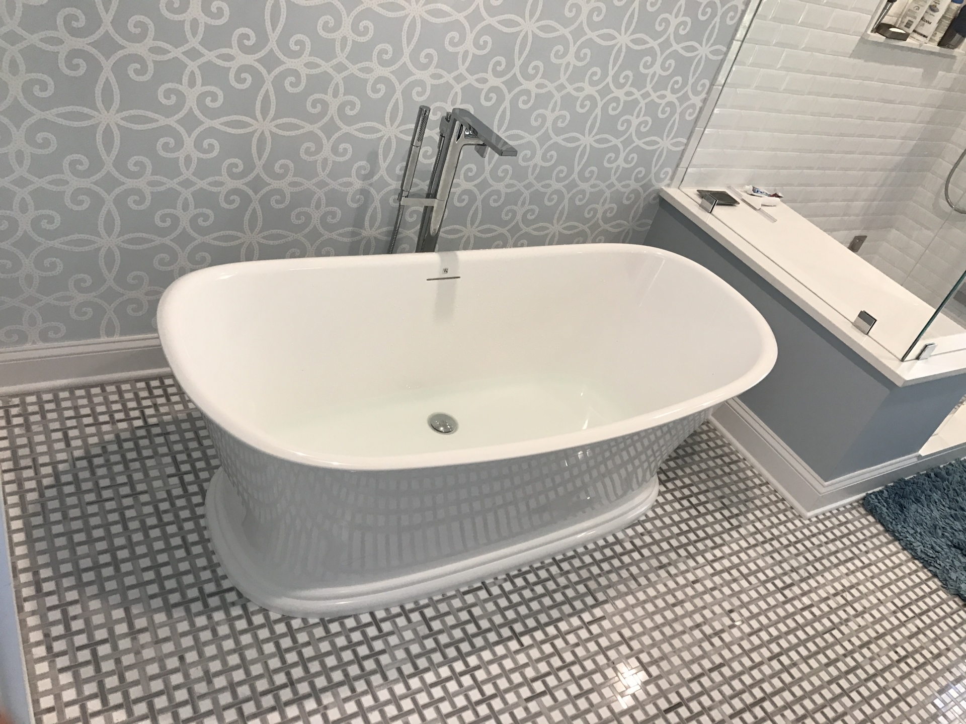 A freestanding soaker tub with a chrome floor-mount filler on a basketweave marble floor