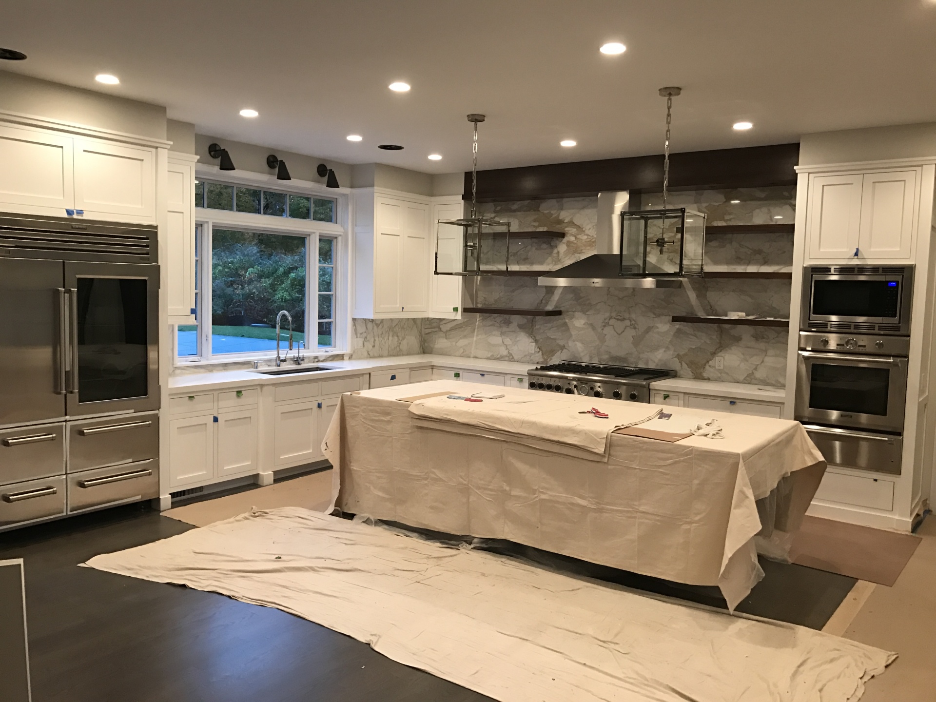 A kitchen being finished out, with a marble slab backsplash, a range and drop cloths still down over the island and floor