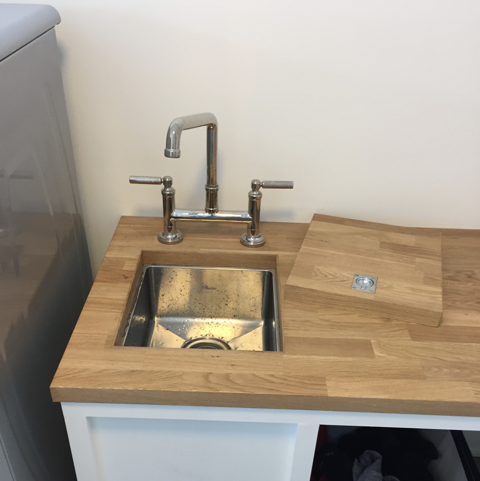 A stainless bar sink undermounted in a butcher block counter with a polished bridge faucet