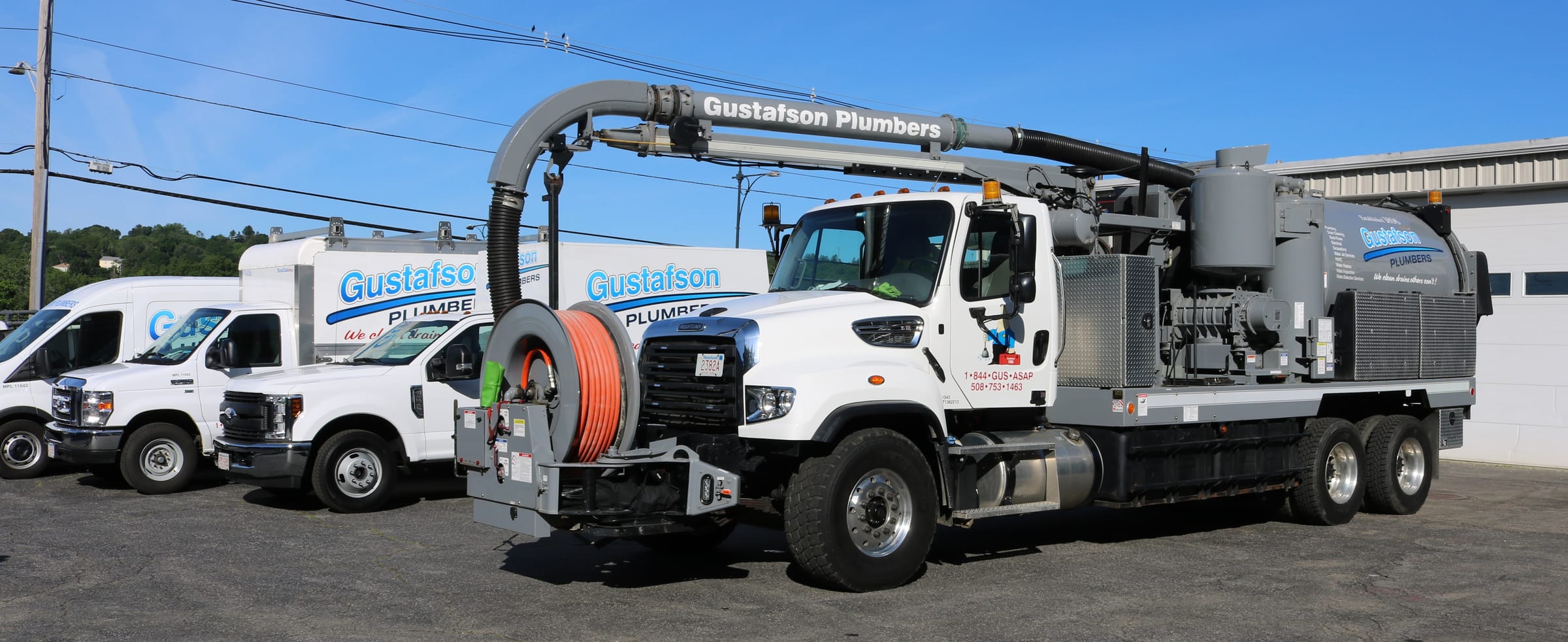 The Gustafson Plumbers vacuum truck with its boom and orange hose reel, branded pickups and box trucks parked behind it