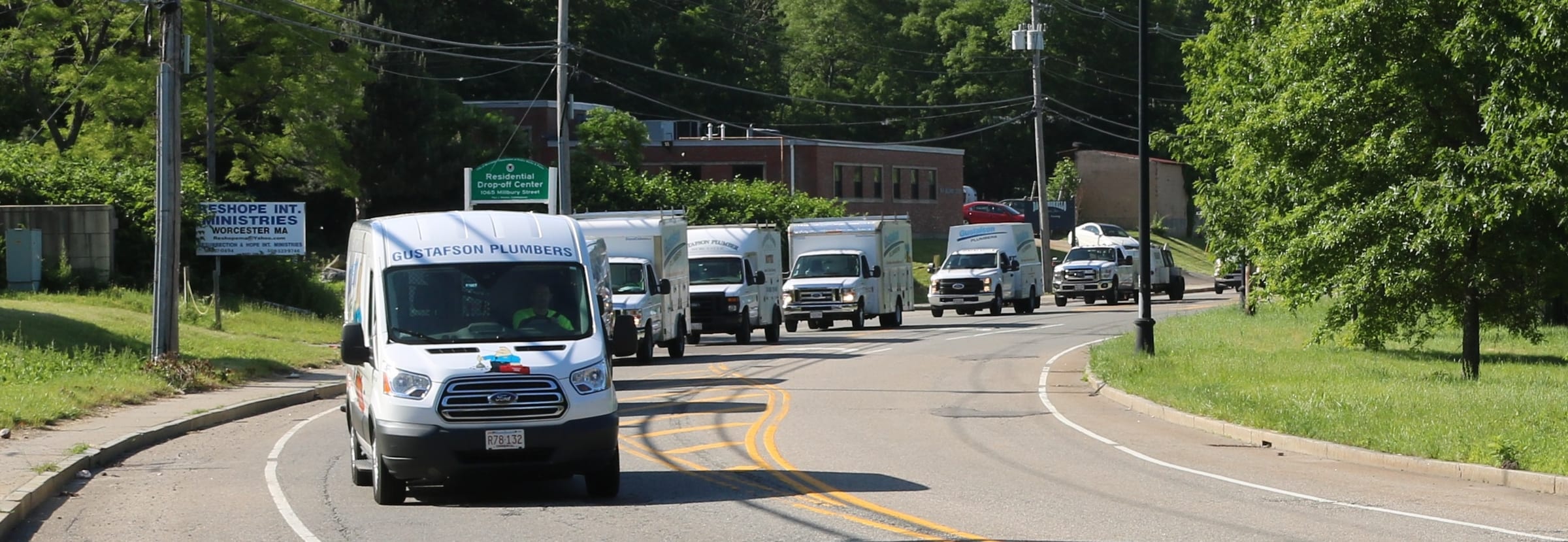 A Gustafson Plumbers van leading a line of vans and box trucks around a curve in Worcester
