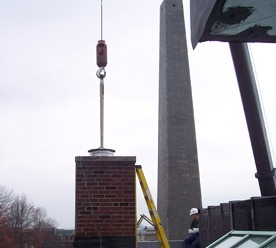 A crane setting a stack section on a brick chimney