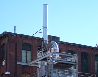 A stainless stack rising from a brick mill roof