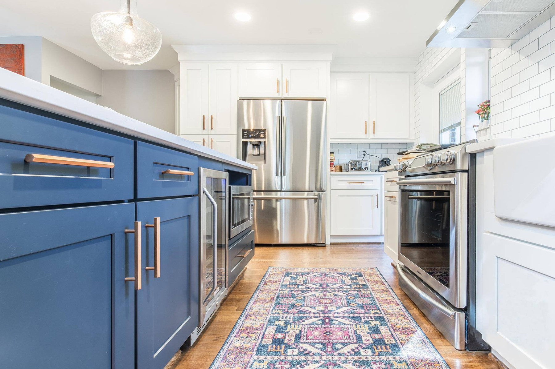 A remodeled kitchen with white upper cabinets, a navy painted island and a warm oak floor