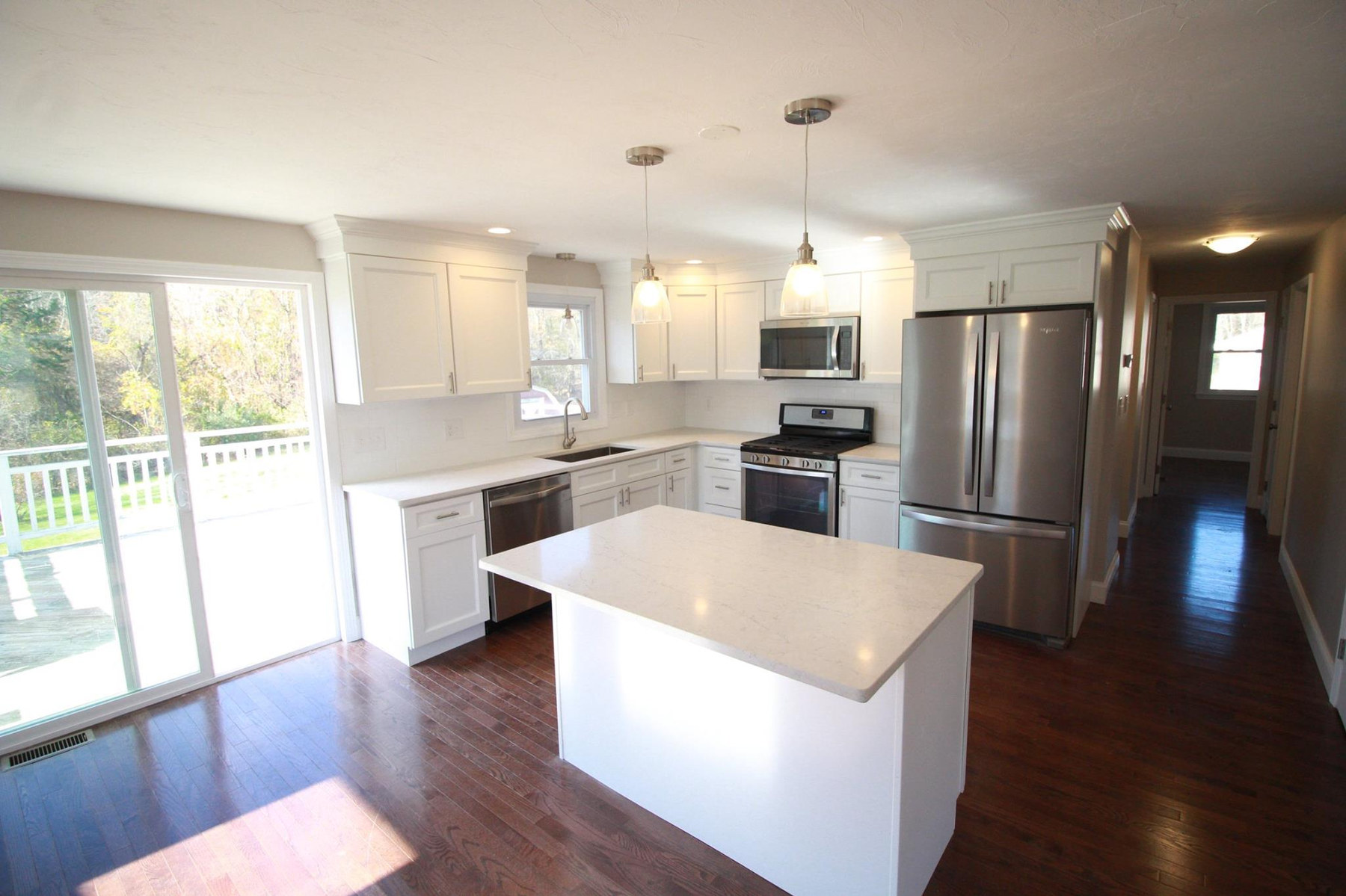 A white kitchen with a quartz island, stainless appliances and a slider out to the deck