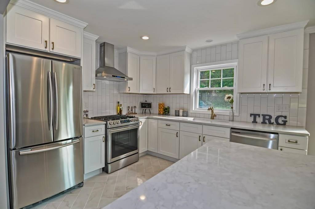 A white kitchen with a marble island and stacked tile behind the range