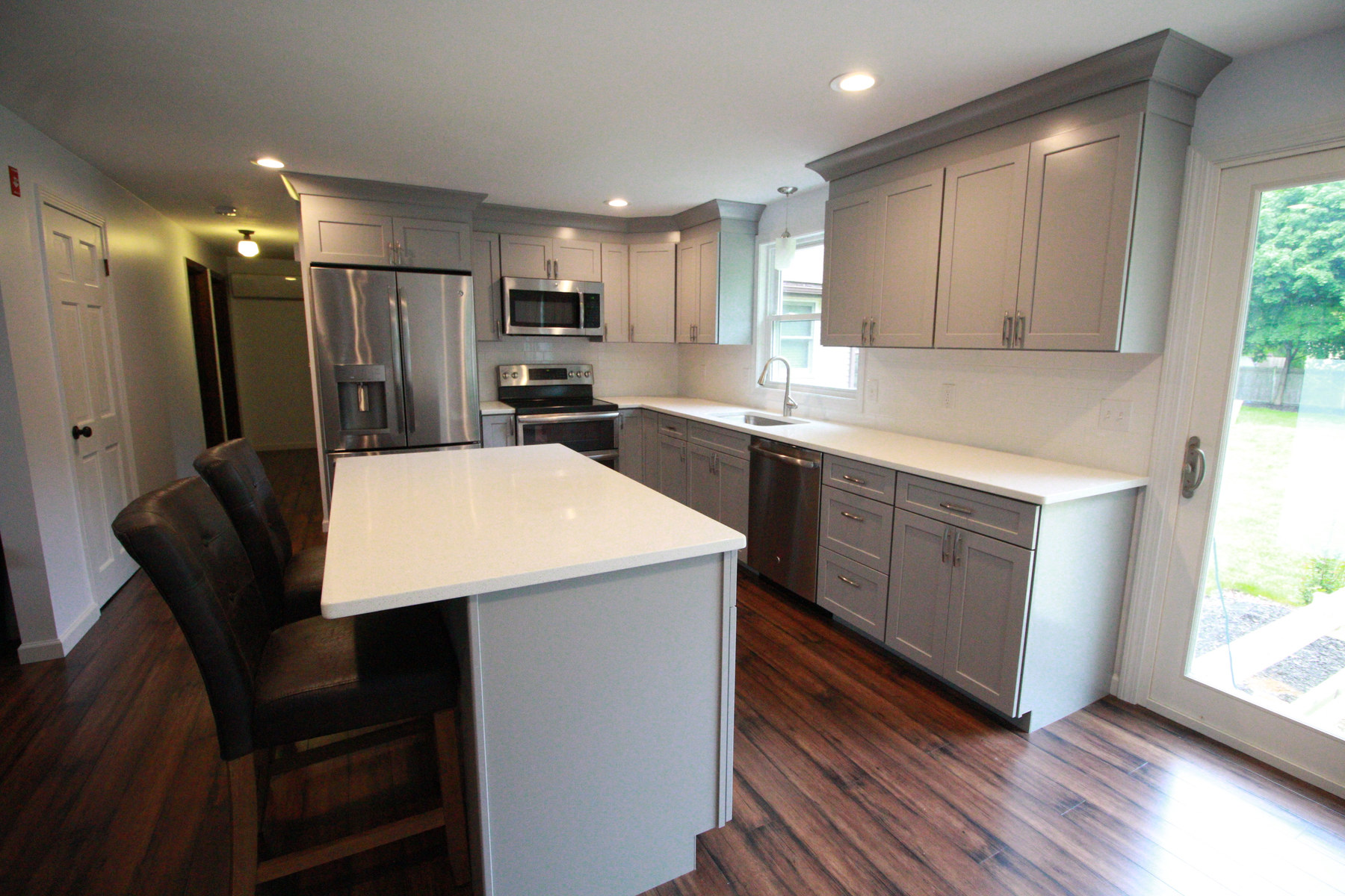 A grey painted kitchen with a white quartz island and leather counter stools