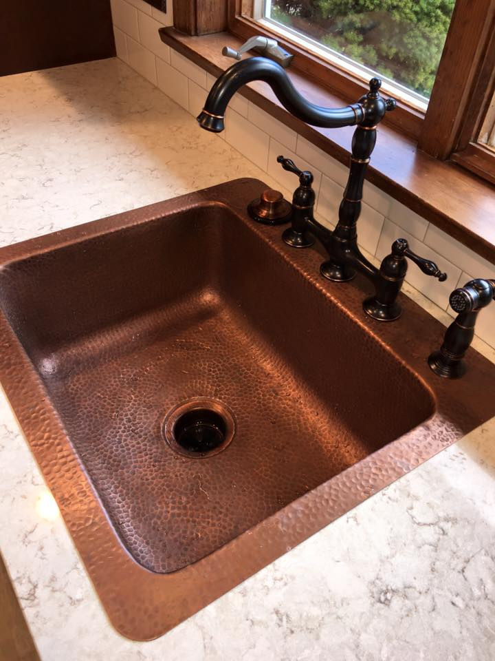 A hammered copper farmhouse sink with an oil rubbed bronze bridge faucet