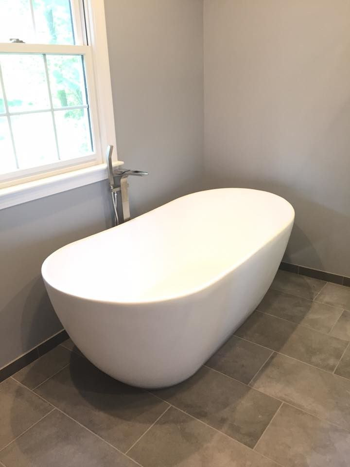 A freestanding soaking tub with a floor mounted filler beside a window