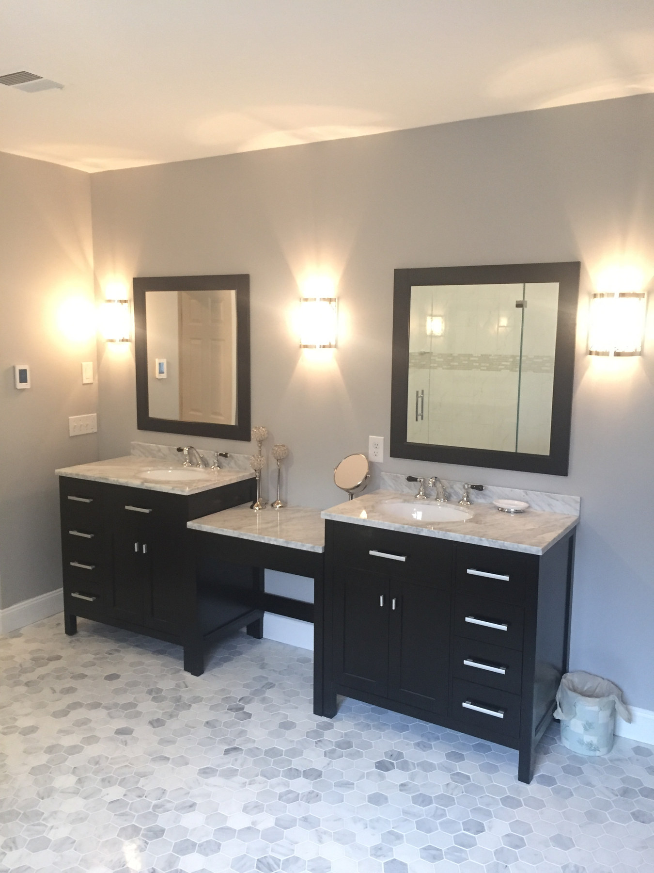 A bathroom with two dark wood vanities, marble tops, sconces and a hexagon tile floor