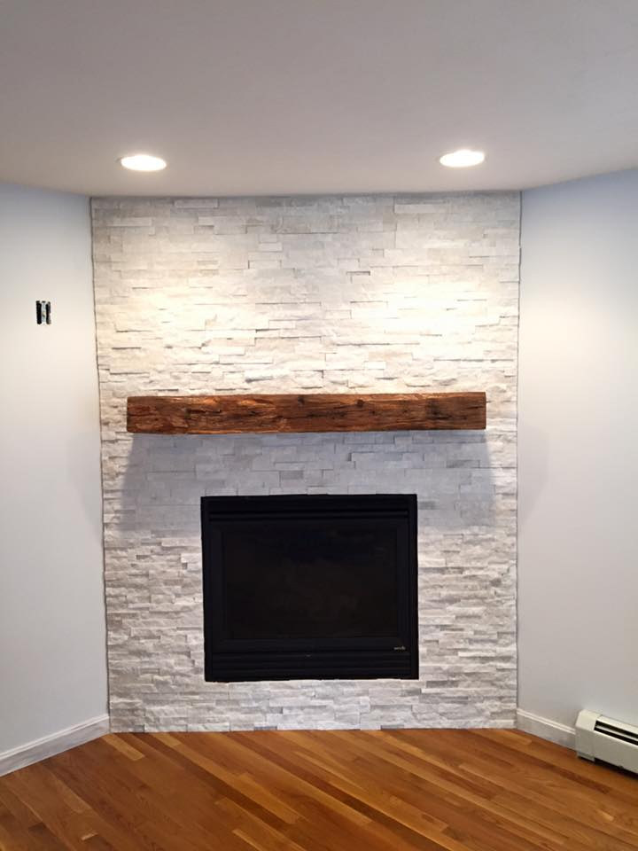 A white stacked stone fireplace with a reclaimed wood beam mantel