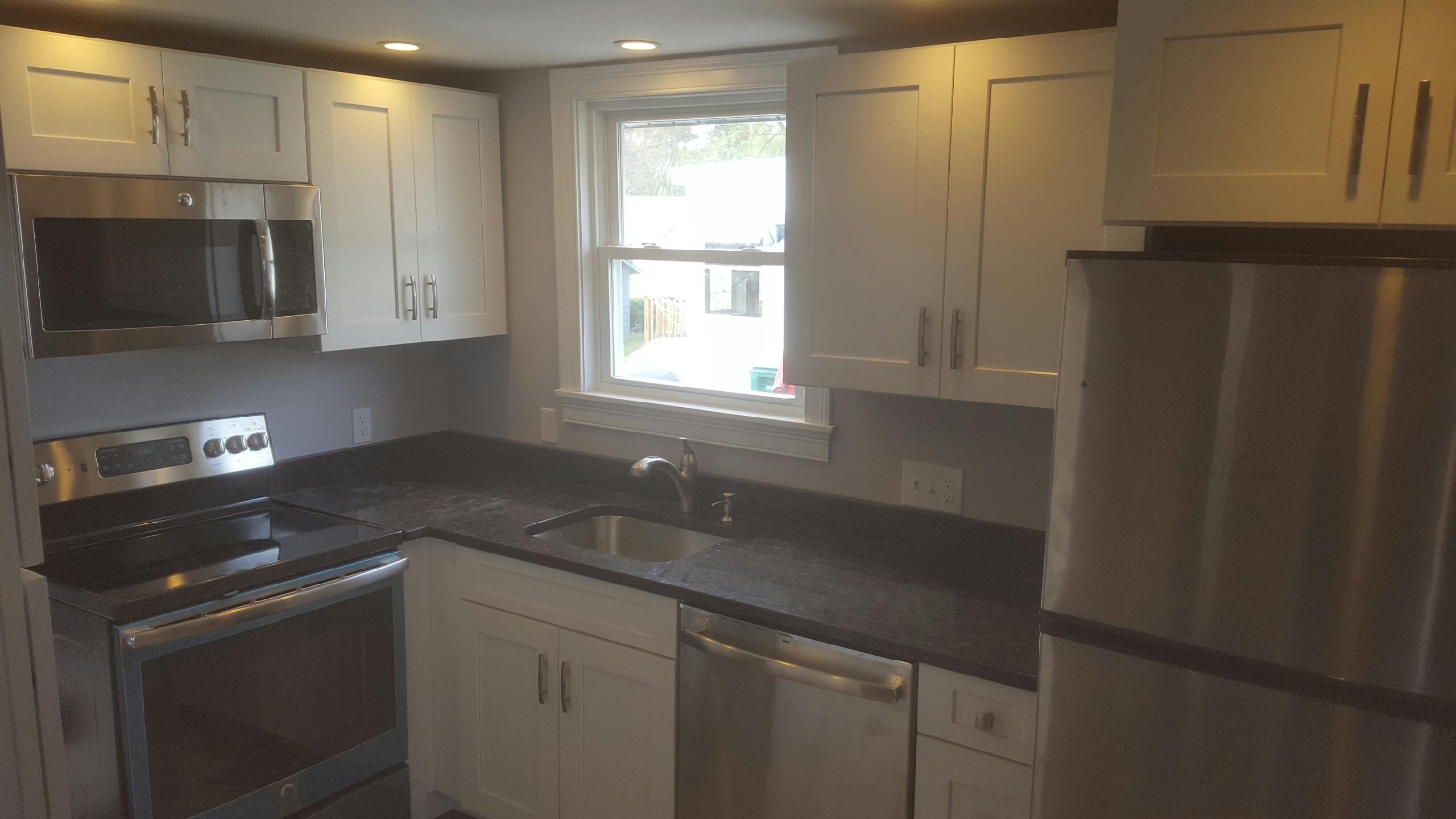 A finished kitchen with white shaker cabinets, dark stone counters and stainless appliances
