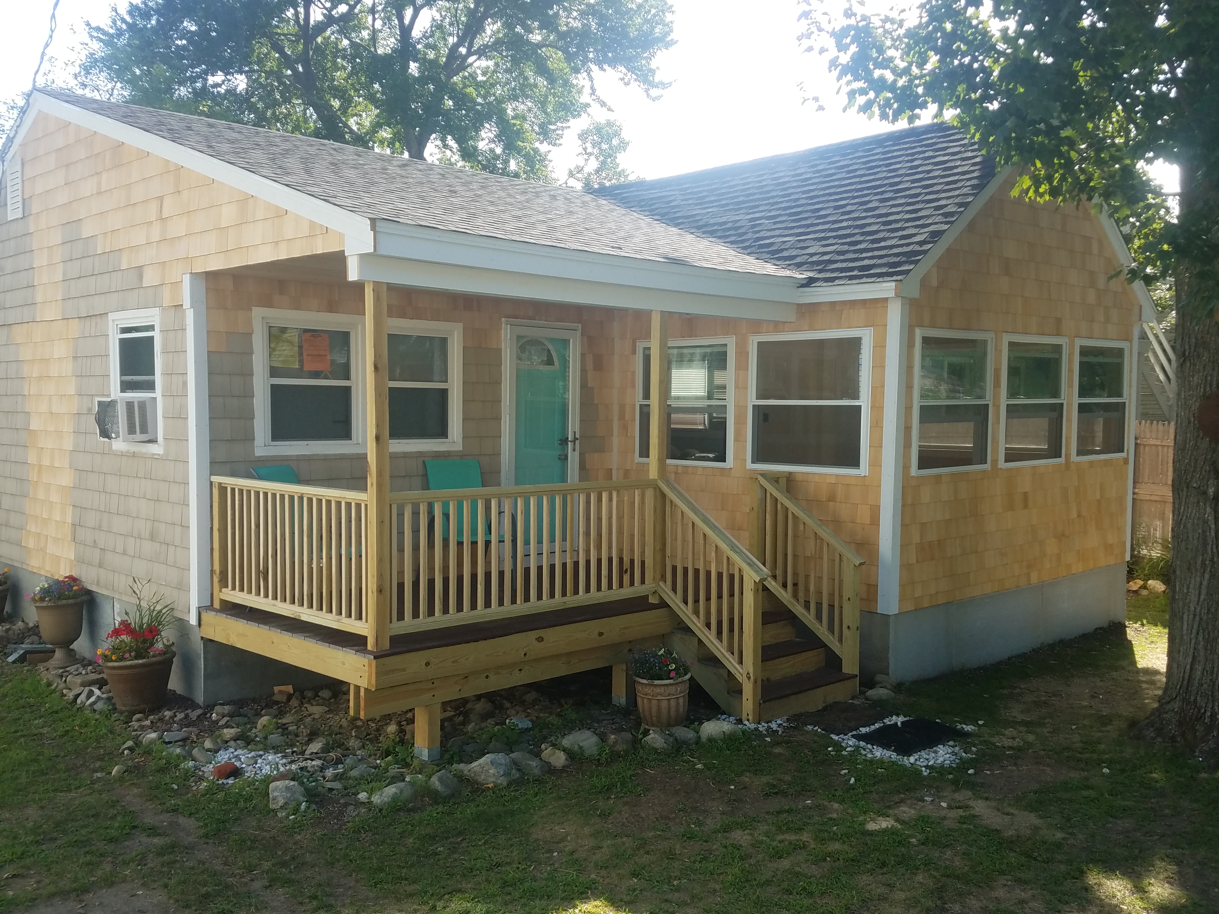 The finished cottage with new cedar shingles, white trim, a teal front door and a new farmer's porch