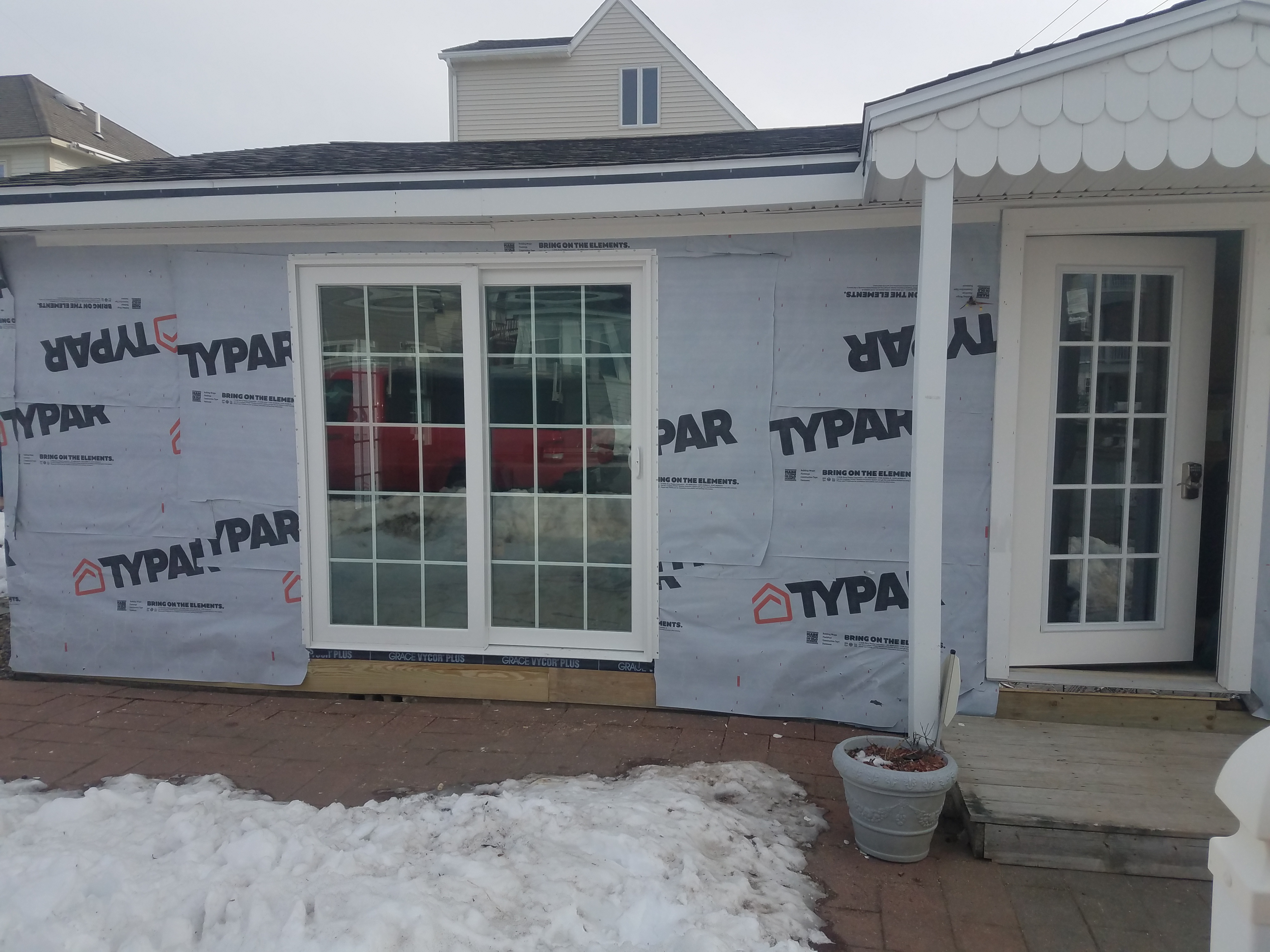 The same wall with a new sliding glass door and a new entry door set in, still wrapped for siding